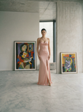 Woman in a blush bustier dress standing in a modern room with abstract art on the walls.