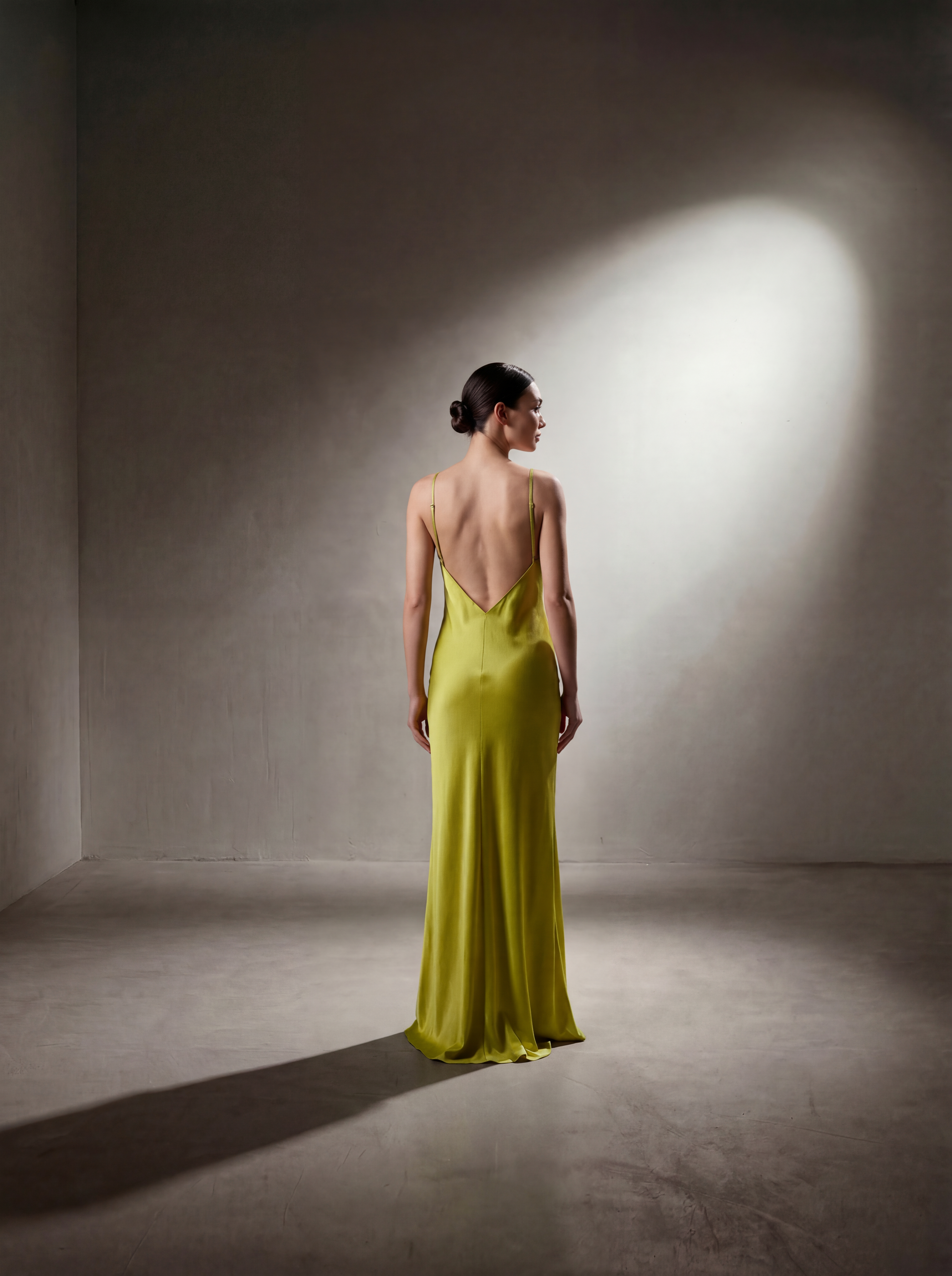 Woman in a green evening gown standing in a dimly lit room with a spotlight.