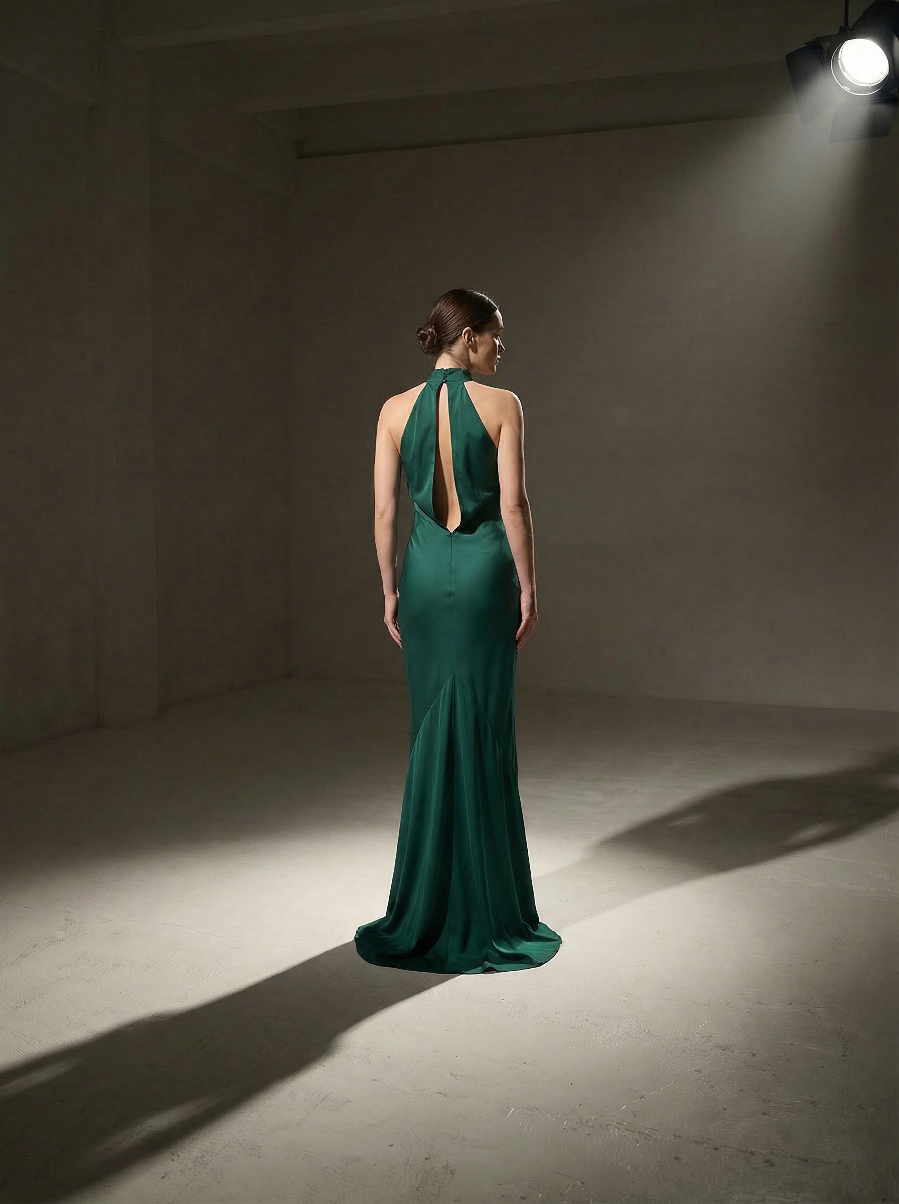 Woman in a pine green silk evening gown standing in a spotlight against a plain background