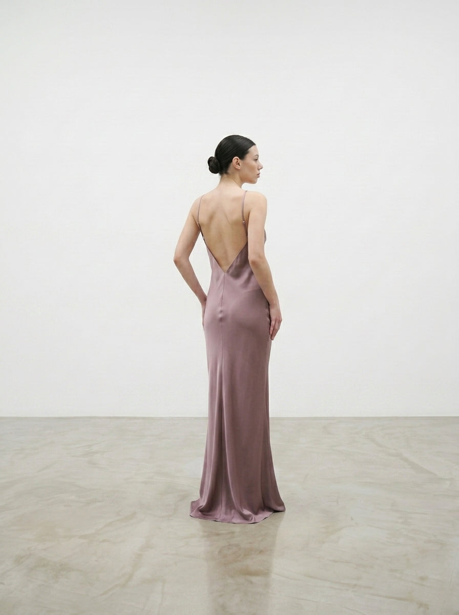 Woman in a backless pink gown standing in a softly lit room.