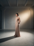 Woman in a beige evening gown standing in a softly lit room.
